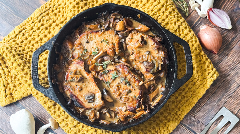 Aromatic smothered pork chops in cast iron skillet on tabletop